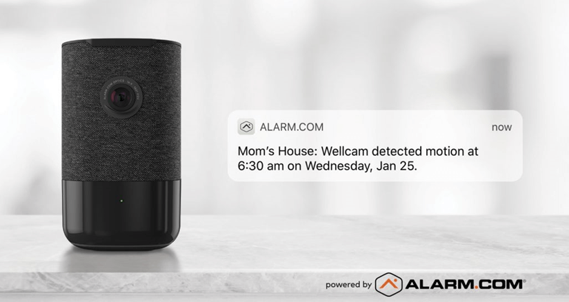 A smart home security camera sits on a marble countertop with a notification from ALARM.COM about motion detected at "Mom's House".