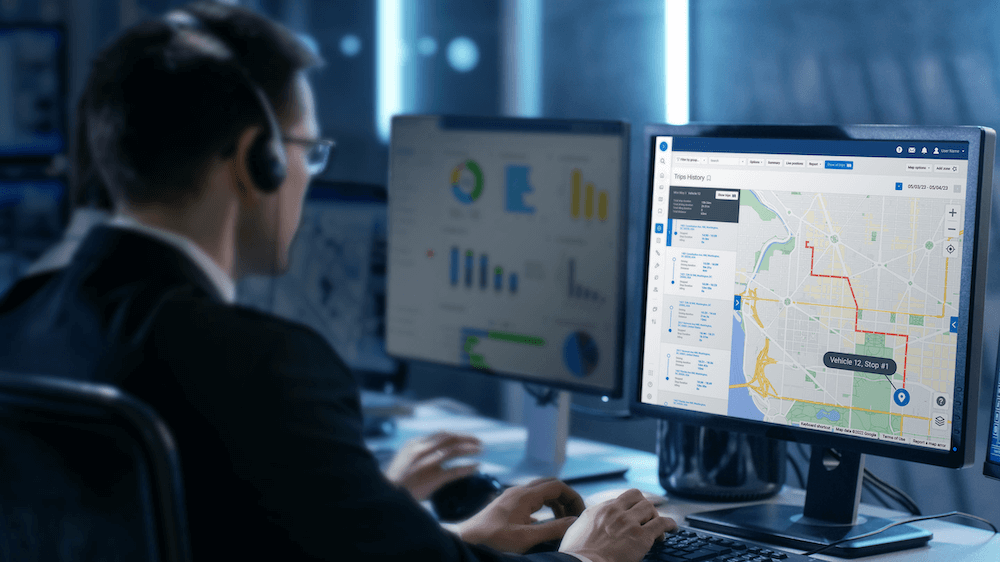 A person is sitting at a desk with multiple monitors displaying graphs and a map, suggesting a focus on data analysis or monitoring activities.